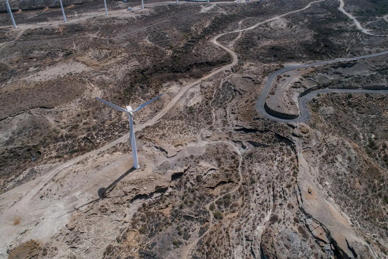 A wind turbine above winding roads in arid hills